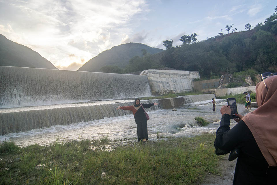 Pengunjung berfoto di depan bendungan air saat berwisata lebaran di Cek Dam Lawara, Desa Balane, Sigi, Sulawesi Tengah, Jumat (12/4/2024). Cek dam yang dibangun Balai Wilayah Sungai Sulawesi (BWSS) III dan telah direhabilitasi itu menjadi salah satu lokasi wisata lebaran yang banyak dikunjungi warga karena memiliki ari terjun dari bendungan juga menyajikan pemandangan sekitarnya yang masih alami. bmzIMAGES/Basri Marzuki