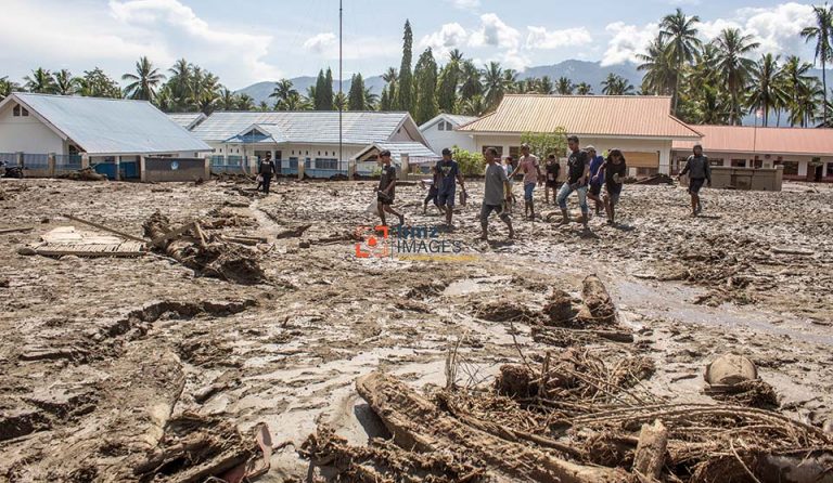 Sejumlah warga berjalan di lapangan desa yang tertutup material lumpur dan serakan potongan batang kayu akibat banjir bandang di Desa Balongga, Kecamatan Dolo Selatan, Kabupaten Sigi, Sulawesi Tengah, Kamis (18/4/2024). Dua desa yakni Desa Balongga dan Desa Sambo di wilayah itu diterjang banjir bandang akibat intensitas hujan yang cukup tinggi di hulu sungai pada Rabu (17/4) malam dan menimbun sejumlah rumah-rumah warga, menghanyutkan ternak dan merusak ratusan hektar lahan pertanian. bmzIMAGES/Basri Marzuki