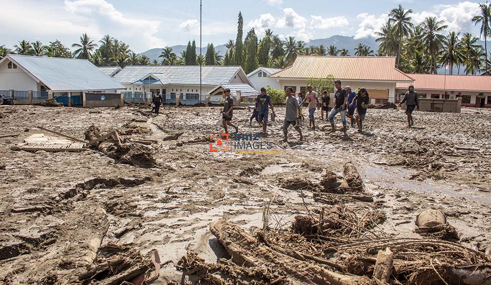 Sejumlah warga berjalan di lapangan desa yang tertutup material lumpur dan serakan potongan batang kayu akibat banjir bandang di Desa Balongga, Kecamatan Dolo Selatan, Kabupaten Sigi, Sulawesi Tengah, Kamis (18/4/2024). Dua desa yakni Desa Balongga dan Desa Sambo di wilayah itu diterjang banjir bandang akibat intensitas hujan yang cukup tinggi di hulu sungai pada Rabu (17/4) malam dan menimbun sejumlah rumah-rumah warga, menghanyutkan ternak dan merusak ratusan hektar lahan pertanian. bmzIMAGES/Basri Marzuki