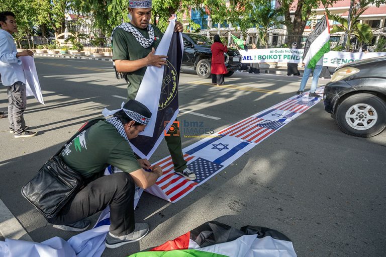 Sejumlah warga yang menamakan diri dari Barisan Aliansi Resistensi Al-Aqsha (Baraq) membentangkan simbol bendera Israel dan Amerika Serikat sebagai alas penyeberangan jalan saat berunjukrasa di Palu, Sulawesi Tengah, Jumat (5/4/2021).