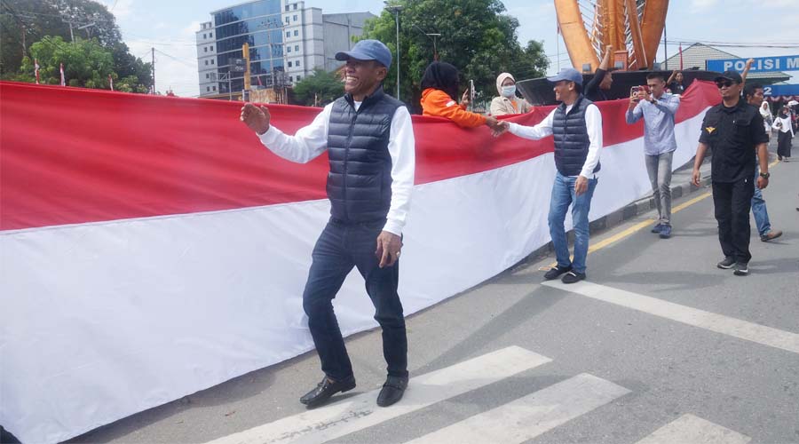 Bakal pasangan calon Wali Kota dan Wakil Wali Kota Palu, Hidayat dan Andi Nur B Lamakarate berjalan di antara bentangan bendera Merah Putih di tugu 0 kilometer, Minggu (18/8/2024). (Foto: Tim Handal)