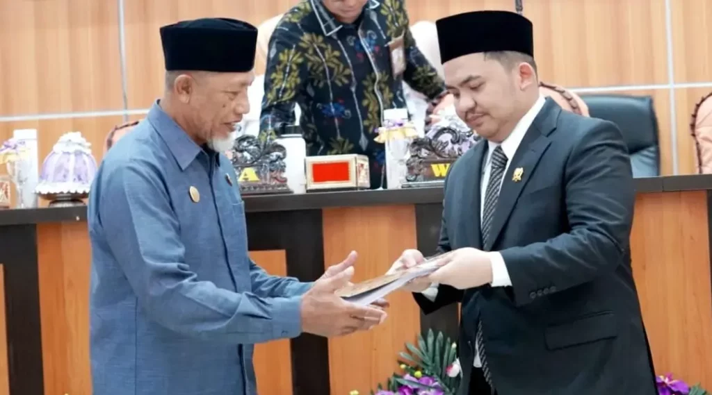 Wakil Ketua DPRD Kota Palu, Moh Anugrah Pratama (kanan) menyerahkan naskah kepada Asisten Bidang Pemerintah dan Kesra Setda Kota Palu pada rapat paripurna DPRD Kota Palu, Rabu (9/10/2024). (Foto: Prokopim Setda Kota Palu/Iwan)