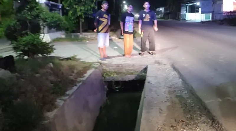 Warga berdiri di dekat got tempat dua mahasiswi terperosok dalam percobaan pembegalan di Jalan Karanjalemba, Senin (17/2/2025) dinihari. (Foto: HUmas Polresta Palu)