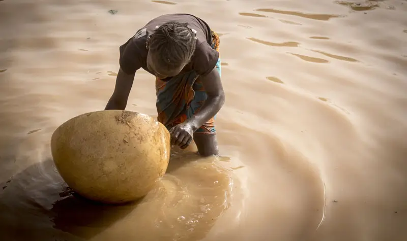 Seorang anak perempuan yang bekerja di lokasi tambang emas Massakama mendulang emas dengan cangkang buah berenuk (calabash). Di wilayah Kayes di Mali, banyak anak yang kehilangan hak-hak dasar mereka atas kesehatan dan pendidikan serta bekerja di lokasi tambang emas. Kayes, 20 Maret 2019. (UNICEF/UN0293787/Keïta)