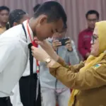 Sekkot Palu Irayanti menyematkan pita kepada peserta tanda dimulainya pemusatan altihan paskibraka 2025. (©Prokopim Setda Kota Palu/Iwan)