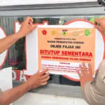Petugas menempel stiker tanda penyegelan tempat usaha yang menunggak pajak di Kota Palu, Selasa (5/8/2025). (©Prokopim Setda Kota Palu/Jufri)