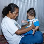 Yuliana Nenotek dan putranya, Sami Sole, 8 bulan, di tempat tidur mereka dilengkapi dengan kelambu anti nyamuk di Desa Maunum, Nusa Tenggara Timur. (©WBW 2025)