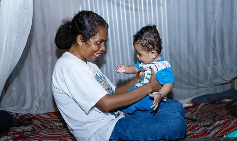 Yuliana Nenotek dan putranya, Sami Sole, 8 bulan, di tempat tidur mereka dilengkapi dengan kelambu anti nyamuk di Desa Maunum, Nusa Tenggara Timur. (©WBW 2025)