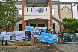 Sejumlah seniman membentangkan spanduk di depan gedung pertunjukan yang rusak di kawaan Taman Budaya Palu, Sabtu (27/9/2025). (© bmzIMAGES/basri marzuki)