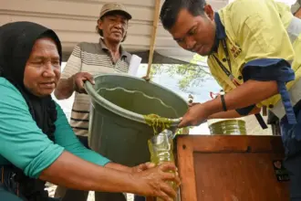Supervisor CSR PT CPM, Zulkifli Salingkat (kanan) membantu petani menuangkan adonan bahan organik ke dalam wadah pada pelatihan pembuatan pupuk organik cair di Kelurahan Poboya, Palu, Sulawesi Tengah, Kamis (2/10/2025). (© bmzIMAGES/basti marzuki)