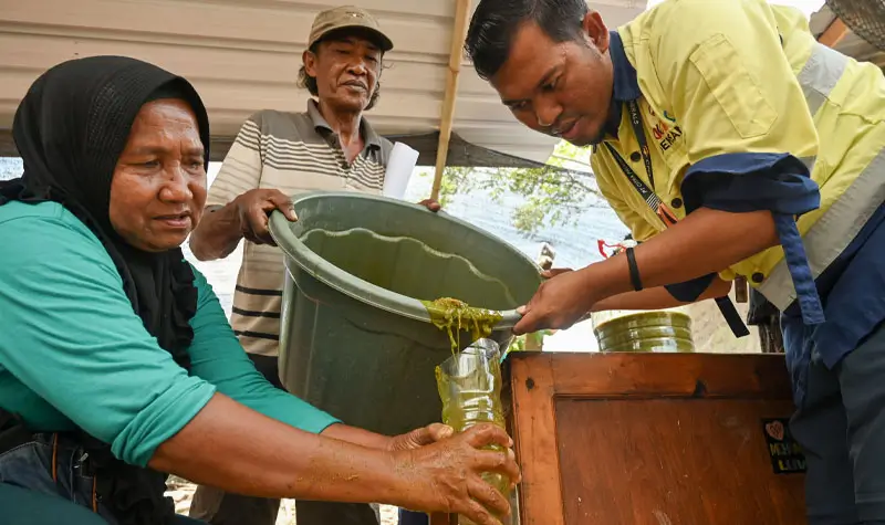 Supervisor CSR PT CPM, Zulkifli Salingkat (kanan) membantu petani menuangkan adonan bahan organik ke dalam wadah pada pelatihan pembuatan pupuk organik cair di Kelurahan Poboya, Palu, Sulawesi Tengah, Kamis (2/10/2025). (© bmzIMAGES/basti marzuki)