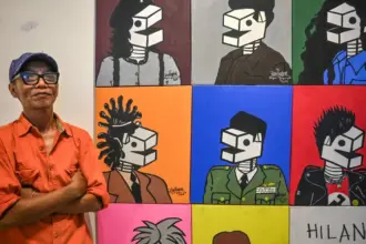 Perupa Wiyoso Yoganingrat alias Iwin berdiri di dekat karya lukisnya pada pameran tunggal di Ondewe Cafe, Palu, Sulawesi Tengah, Senin (17/11/2025) malam. ©bmzIMAGES/Basri Marzuki)