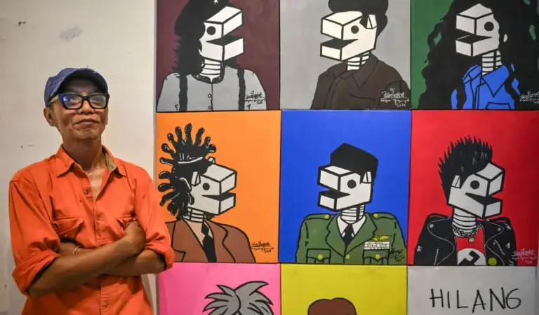 Perupa Wiyoso Yoganingrat alias Iwin berdiri di dekat karya lukisnya pada pameran tunggal di Ondewe Cafe, Palu, Sulawesi Tengah, Senin (17/11/2025) malam. ©bmzIMAGES/Basri Marzuki)