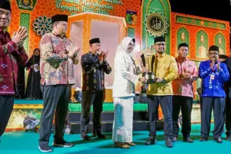 Asisten Administrasi Umum Setda Kota Palu, Eka Komalasari menyerahkan piala kepada kontingan Palu Selatan yang meraih juara umu pada MTQ ke-28 di Tipo, Ulujadi, Rabu (4/11/2025). (©Prokopim Setda Kota Palu/Yuspi)