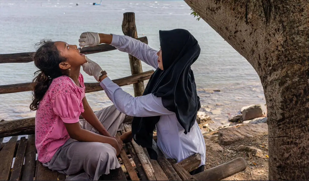 Rani Amsa, bidan dari Puskesmas Peukan Bada, memberikan imunisasi polio di dekat pantai di Aceh Besar, Aceh, saat Pekan Imunisasi Nasional pada bulan Desember 2022. (©WHO/Fauzan Ijazah)