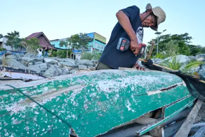 Eri menambal perahunya yang sudah lapuk dimakan usia, Selasa (3/2/2026). (©bmzIMAGES/Basri Marzuki)