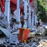 Warga berada di dekat reruntuhan gedung akibat gempa 7.6 M di Manado, Kamis (2/4/2026). (©AFP/Tonny Rarung/CNN)