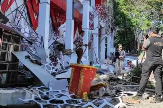 Warga berada di dekat reruntuhan gedung akibat gempa 7.6 M di Manado, Kamis (2/4/2026). (©AFP/Tonny Rarung/CNN)
